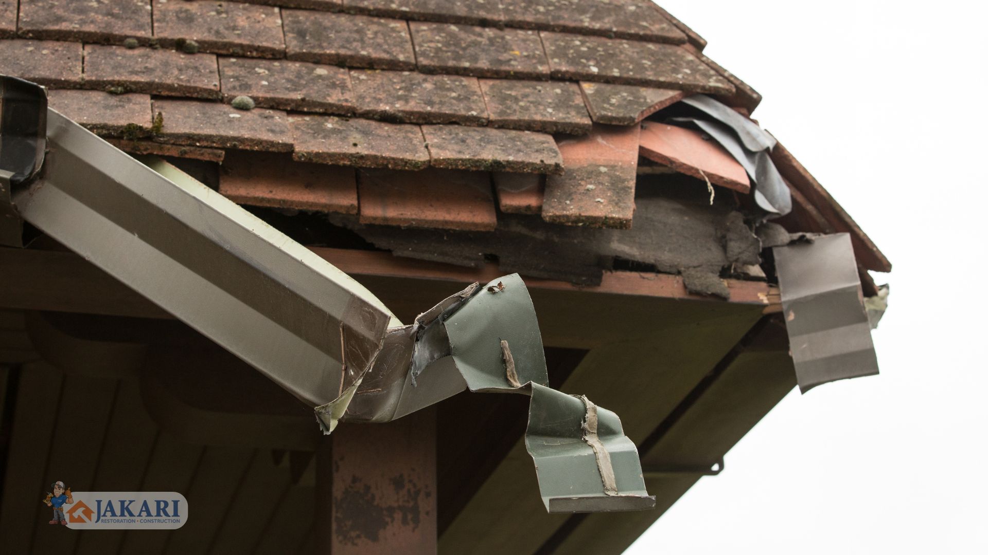 A close-up of a house roof shows damaged shingles, exposed wood, and bent metal flashing near the eaves. The roof appears weathered and in need of repair.
